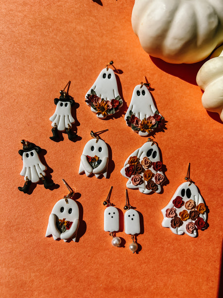 Halloween-themed earrings on an orange background with pumpkins.